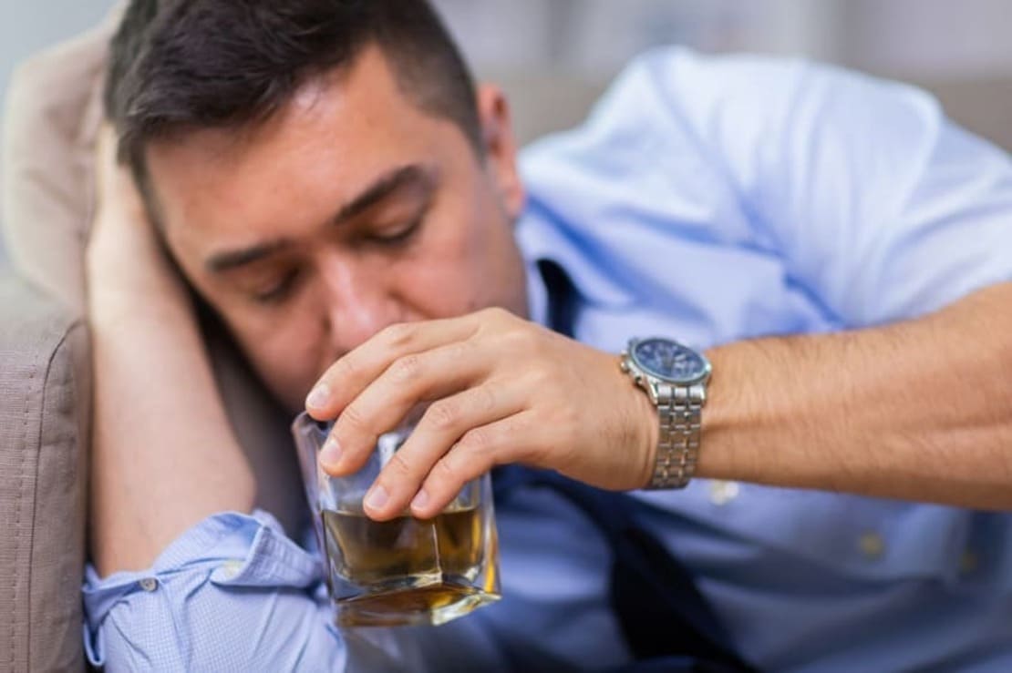 Мужчина с дерматитом пьет алкоголь из стакана
